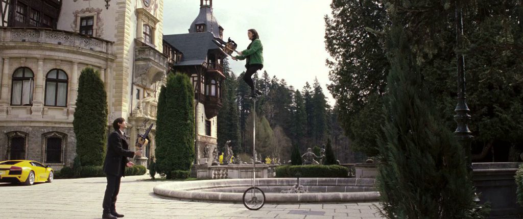 Penelope holds two chainsaws while sitting on a unicycle, telling Bloom to throw a third chainsaw up to her to juggle.